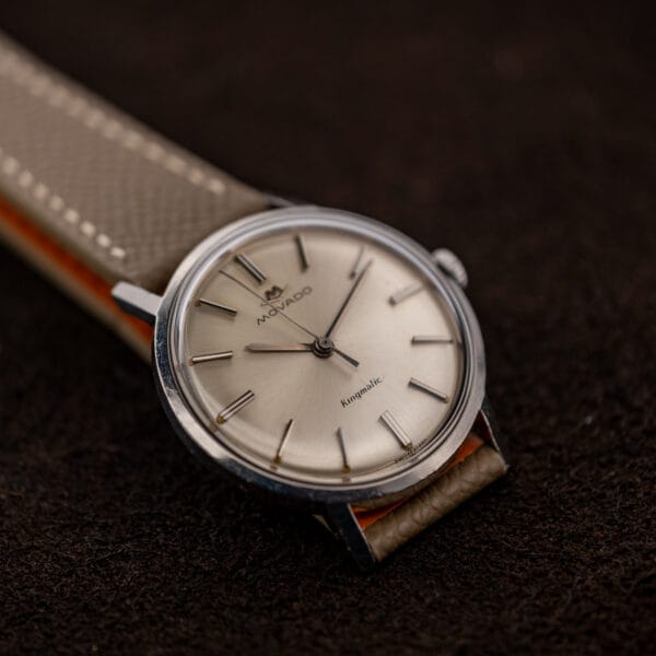 Movado Kingmatic 15161 viewed across the lower lugs, with its sunburst dial and taupe strap angled left