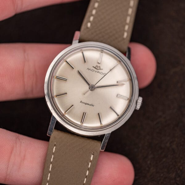 Hand-held Movado Kingmatic 15161 displaying its three-hand dial, applied hour markers and stitched taupe leather strap