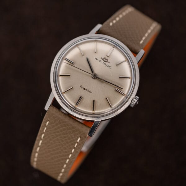 Angled Movado Kingmatic 15161 with crown at lower right and the taupe leather strap curved behind