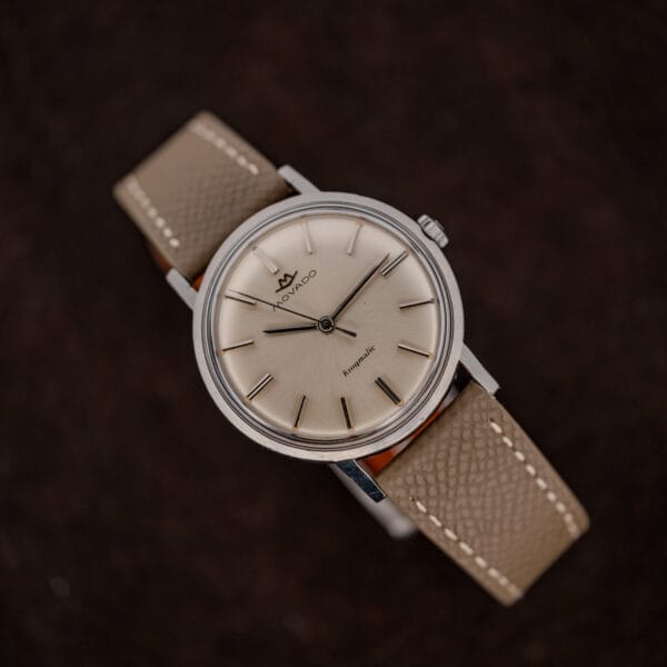 Movado Kingmatic 15161 with the crown at upper right and its taupe leather strap curving below the dial