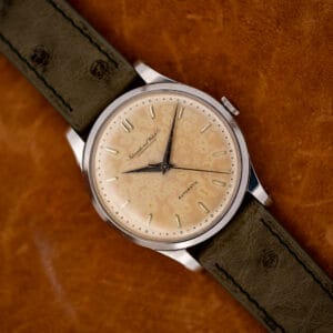IWC automatic with mottled eggshell dial and olive ostrich strap resting diagonally on orange fabric