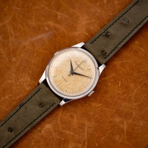 IWC stainless steel automatic shown face-up with its olive ostrich strap extended across orange cloth