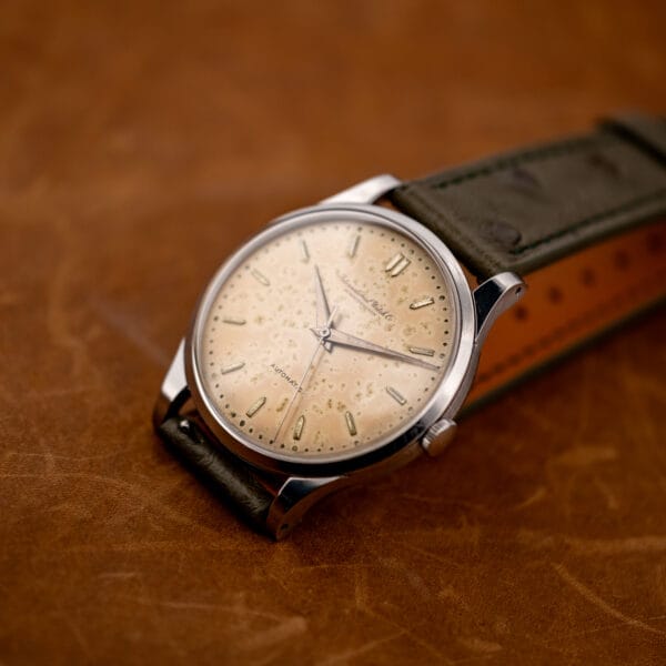 IWC automatic resting on its folded ostrich strap, with the patina dial and crown facing forward