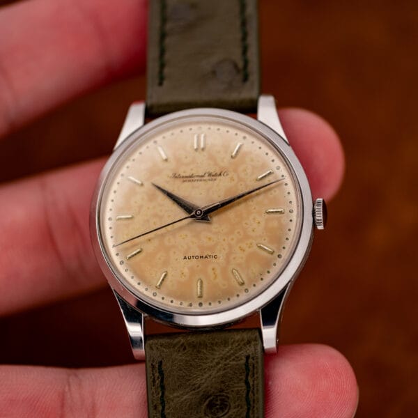 Hand-held IWC at a slight angle, with the crown, smooth bezel and patina dial in view
