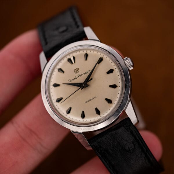 Hand-held Girard Perregaux Gyromatic showing white dial, central seconds and smooth bezel