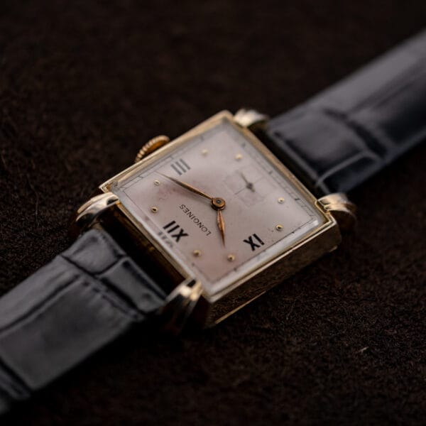 Low oblique Longines dial view highlighting curved crystal, pointed hands and sculpted corner lugs