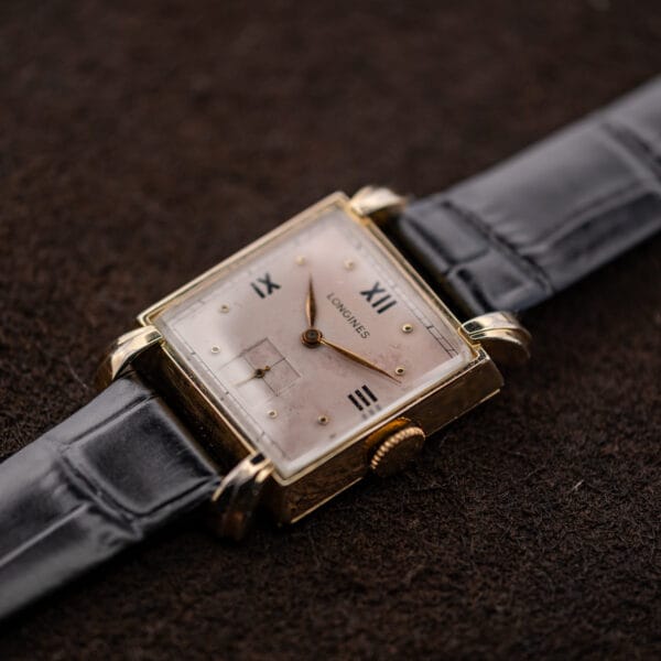 Crown-side Longines portrait showing rose dial, square seconds register and black leather strap