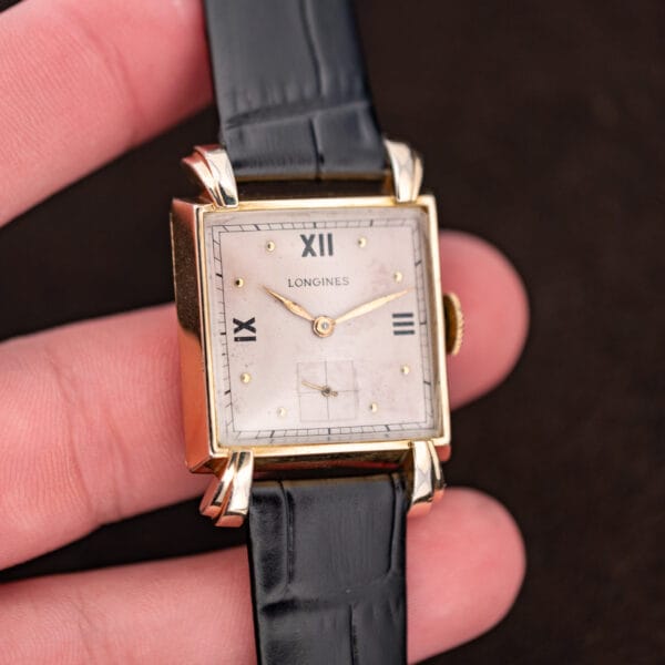 Handheld front view of Longines square dress watch with Roman numerals and black leather strap