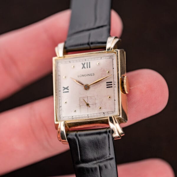 Longines held in hand showing rose dial, gold filled square case and crown-side detail
