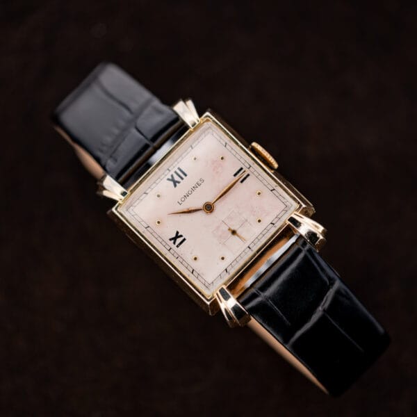 Longines square rose dial and flared lugs displayed above a curved black leather strap