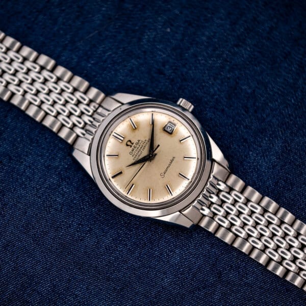Full Omega Seamaster 168.024 laid face-up with its stainless steel bracelet extended across blue cloth
