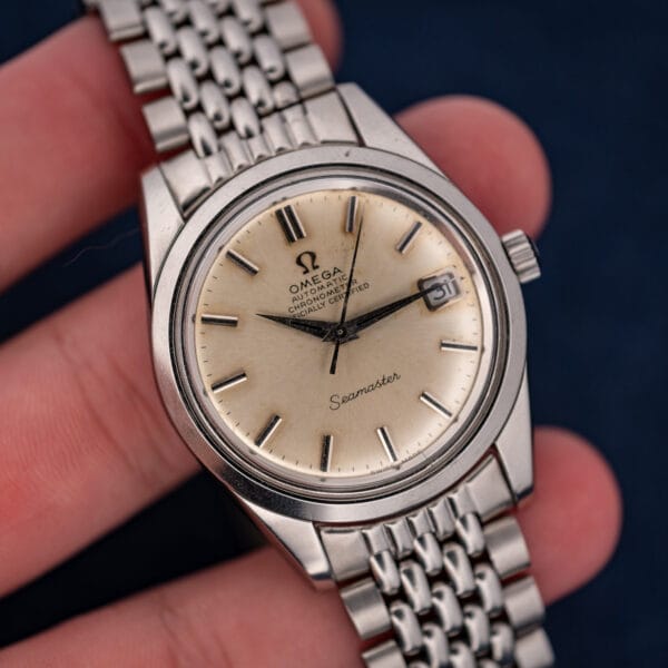 Omega Seamaster 168.024 held across fingers, showing the complete dial, date window and stainless steel bracelet