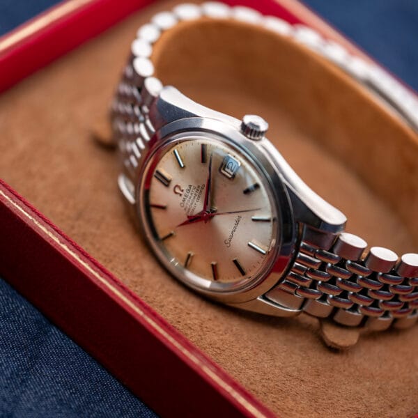 Omega Seamaster 168.024 displayed on a tan cushion with its steel bracelet curved around the support