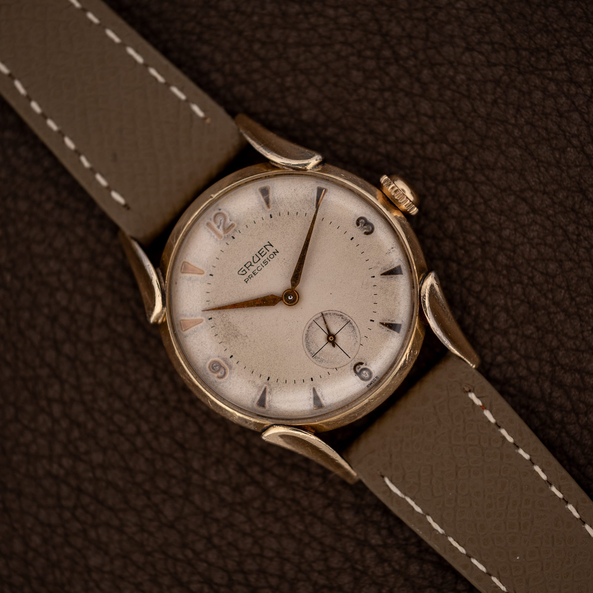 DSCF7193 Gruen Precision 415/932 with curved fancy lugs and taupe leather strap resting diagonally on a textured brown surface