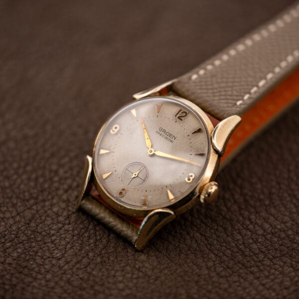 Gruen Precision 415/932 angled on a brown surface with its smooth bezel, small seconds and taupe strap