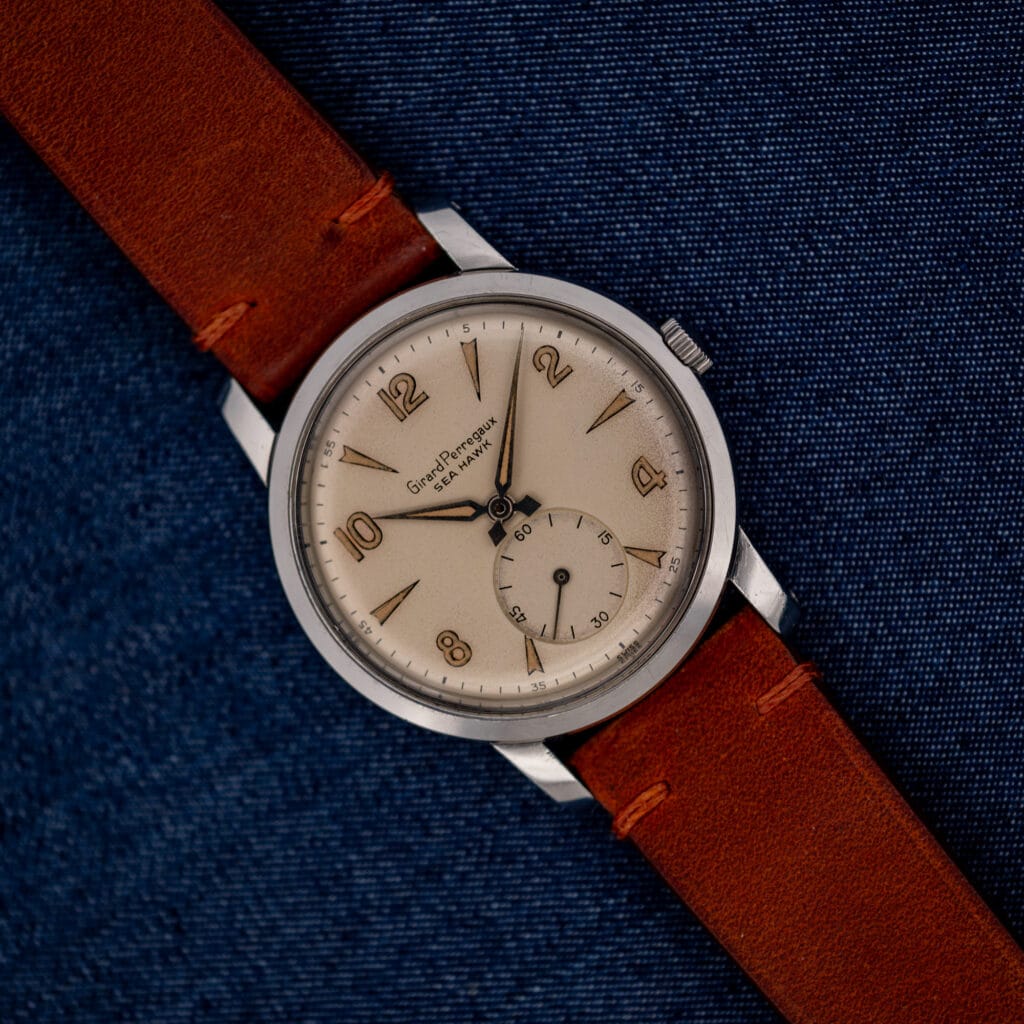 Girard Perregaux Sea Hawk with eggshell dial and brown leather strap resting diagonally on blue fabric