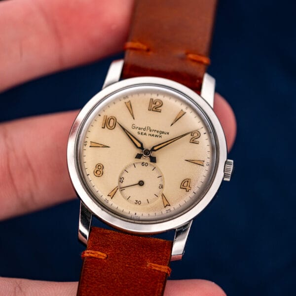 Girard Perregaux Sea Hawk held upright between fingers, displaying the eggshell dial and small seconds