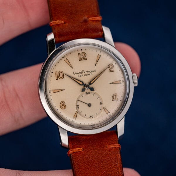 Hand-held Girard Perregaux Sea Hawk at a slight angle, with brown leather strap above and below the case