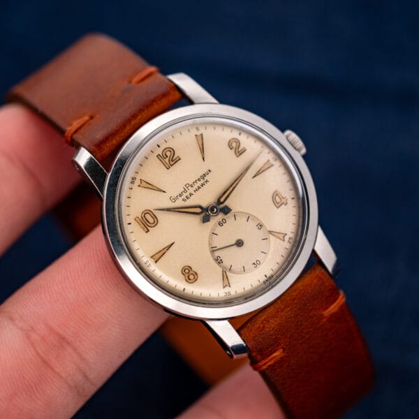 Girard Perregaux Sea Hawk held between fingers with its strap curved, showing the full dial and crown
