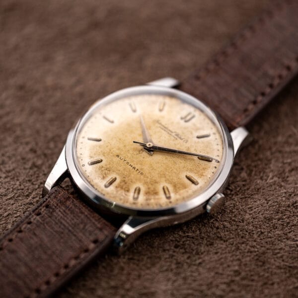 Low crown-side IWC view highlighting raised crystal, dauphine hands and curved lugs