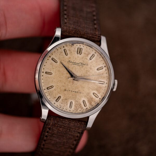 Hand-held IWC frontal view showing paired twelve markers and finely dotted minute track