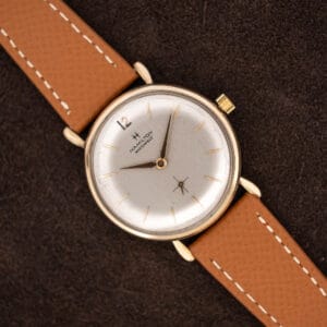 Hamilton Masterpiece with silver dial and tan stitched leather strap lying diagonally across brown fabric