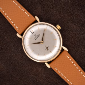 Hamilton Masterpiece with silver dial and tan stitched leather strap lying diagonally across brown fabric