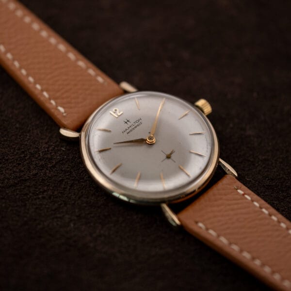 Hamilton Masterpiece viewed obliquely with the crown above the dial and tan strap running toward the lower right