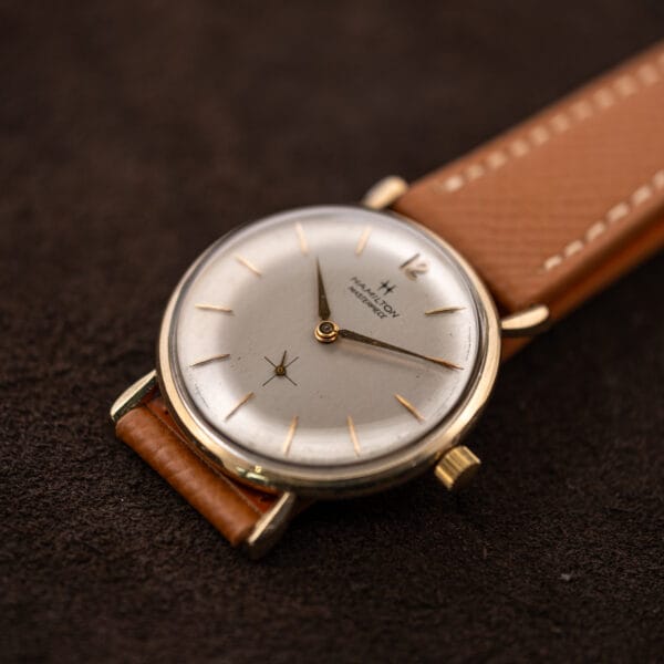 Hamilton Masterpiece resting on its folded tan strap, with the small seconds and lower lugs visible