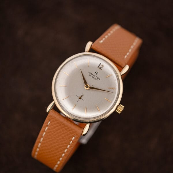 Hamilton Masterpiece elevated on a curved tan strap, its applied twelve toward the upper right