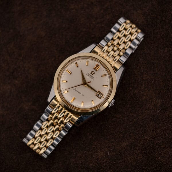 Omega Seamaster 14744-1 resting on brown fabric with its bracelet curved beneath the white dial