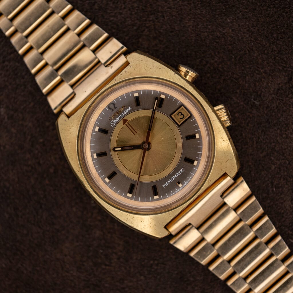 Omega Seamaster Memomatic 166.072 with gold and anthracite dial and linked bracelet resting diagonally on brown fabric