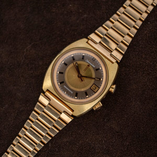 Overhead view of Omega Seamaster Memomatic 166.072 with its gold bracelet extended across brown fabric