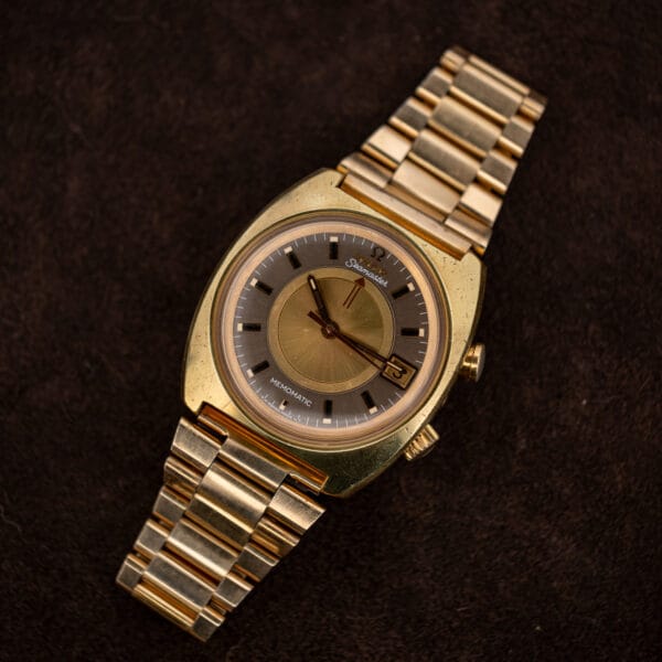 Full Omega Memomatic 166.072 laid diagonally with gold bracelet extended and central alarm discs visible