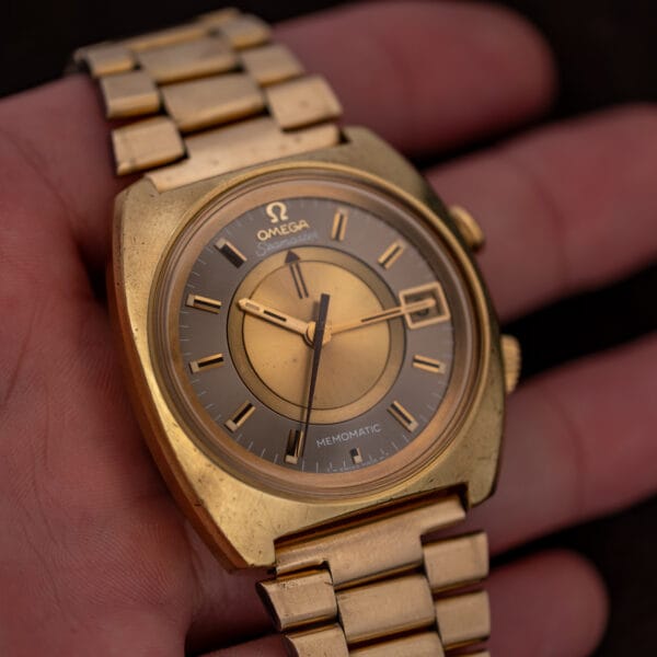 Omega Memomatic 166.072 resting across fingers, showing the gold and anthracite dial and bracelet ends