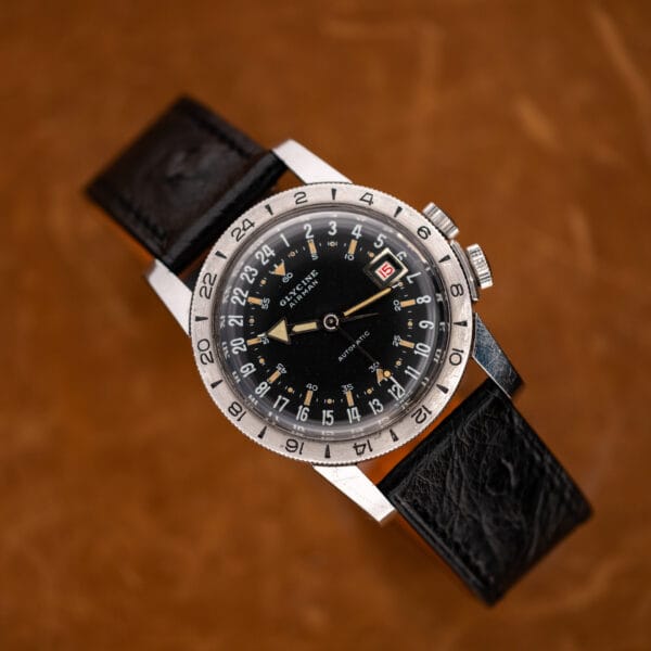 Glycine Airman angled above a brown surface, with the black strap curved underneath and full dial visible