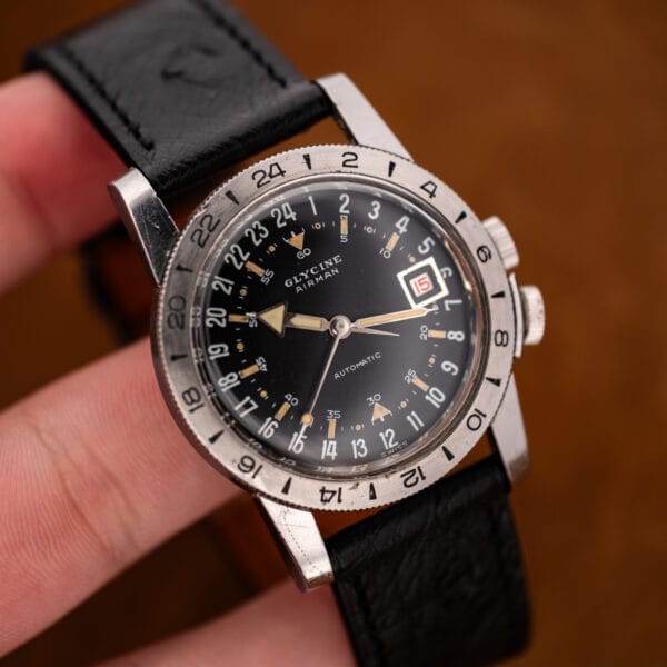 Hand-held Glycine Airman showing the broad arrow hand, red date and black ostrich strap at an angle