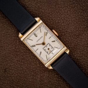 Longines Art Deco tank with off-white dial, Arabic numerals and black leather strap on a brown surface