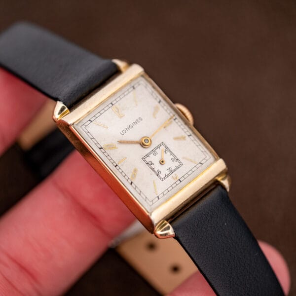 Hand-held Longines Art Deco tank tilted toward the light, showing its gold-filled case and black leather strap