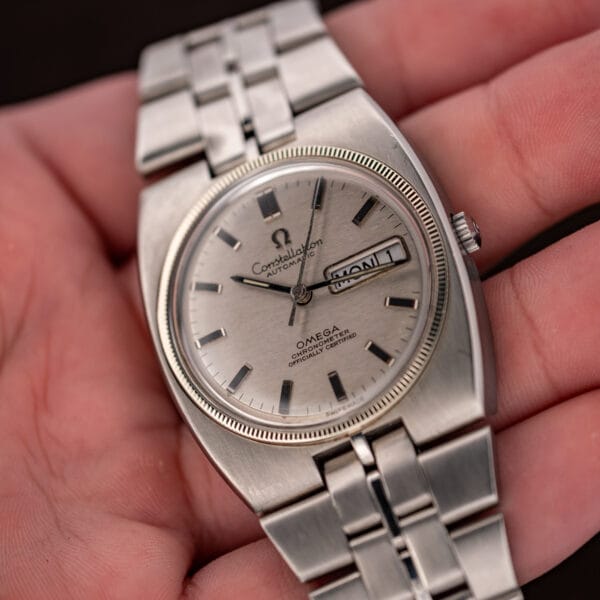In-hand oblique Constellation view highlighting dark baton indices, coin-edged bezel and crown-side case shoulder