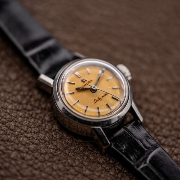 Low oblique Omega Ladymatic view showing lemon dial texture, applied indices and black leather strap