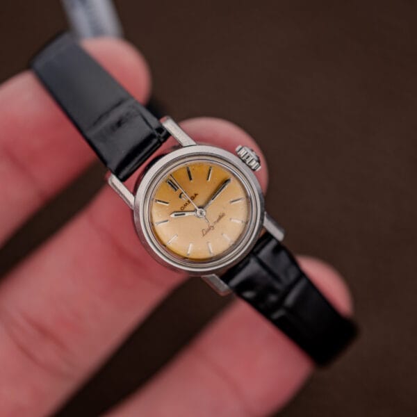 Omega Ladymatic held above fingertips, showing small round case, central seconds and lemon dial