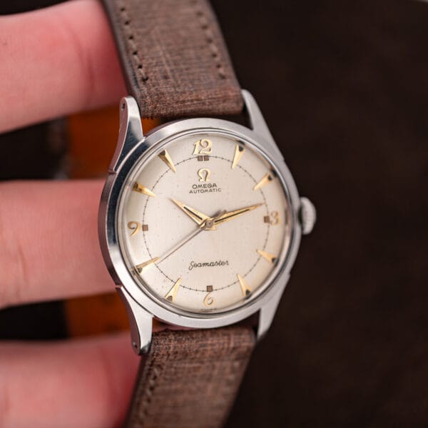 Handheld Omega Seamaster 2635-9 SC showing its eggshell dial, Arabic quarter numerals, and textured brown strap