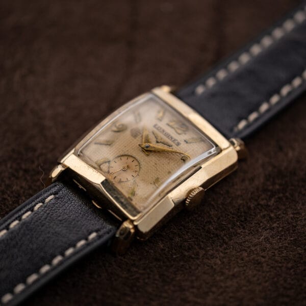Crown-side oblique Longines view showing raised crystal, faceted gold filled case and textured dial