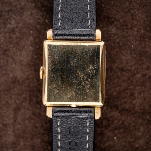 Longines exterior square caseback stamped 10K GOLD FILLED above a black stitched leather strap