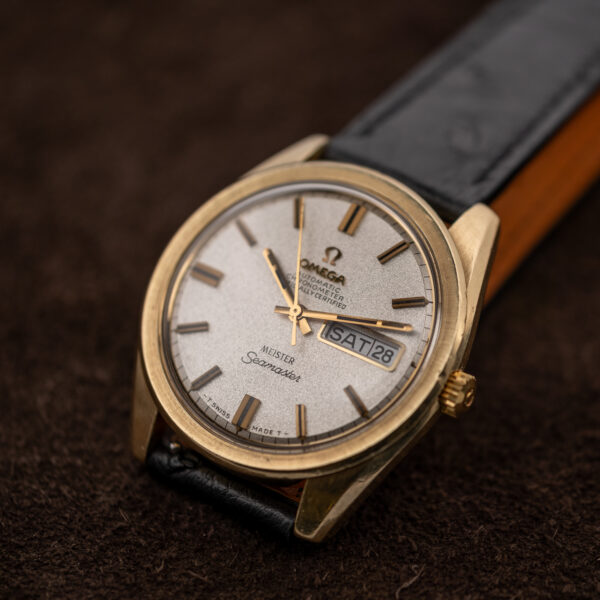 Omega Seamaster angled portrait showing Meister lettering, day-date aperture and contrasting strap lining beside the case