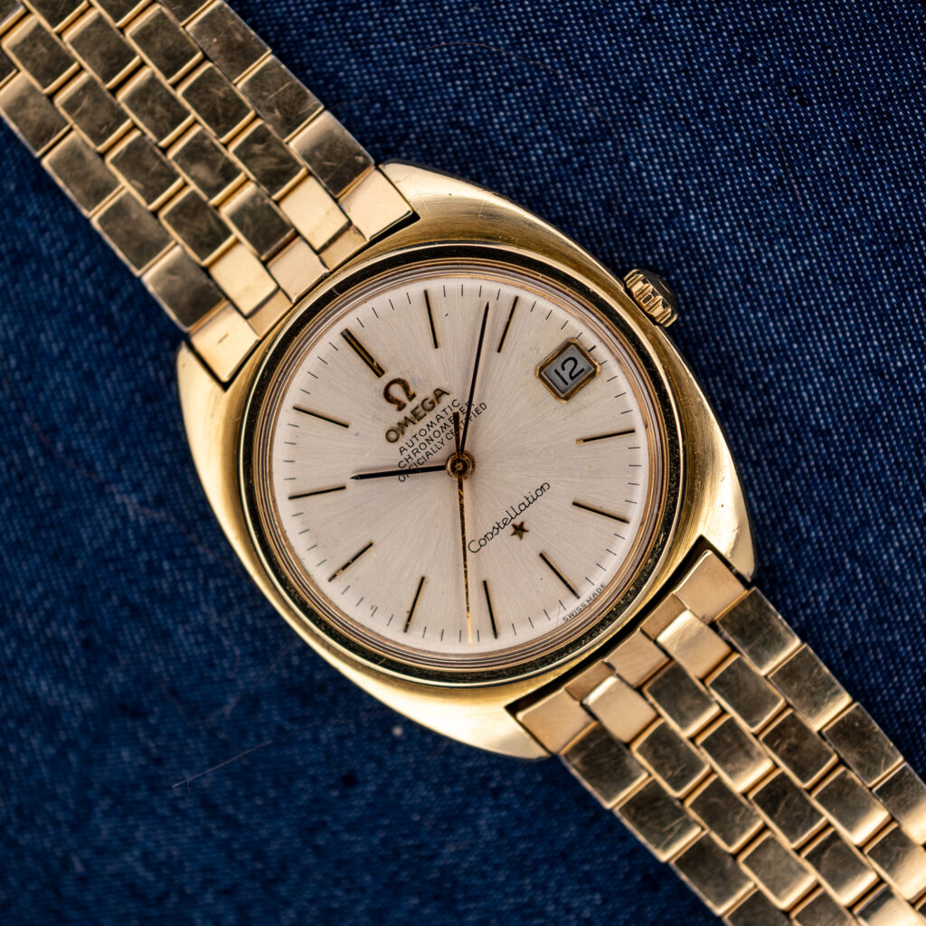 Omega Constellation 168.017 overhead view with silver dial, framed date and linked bracelet on navy fabric