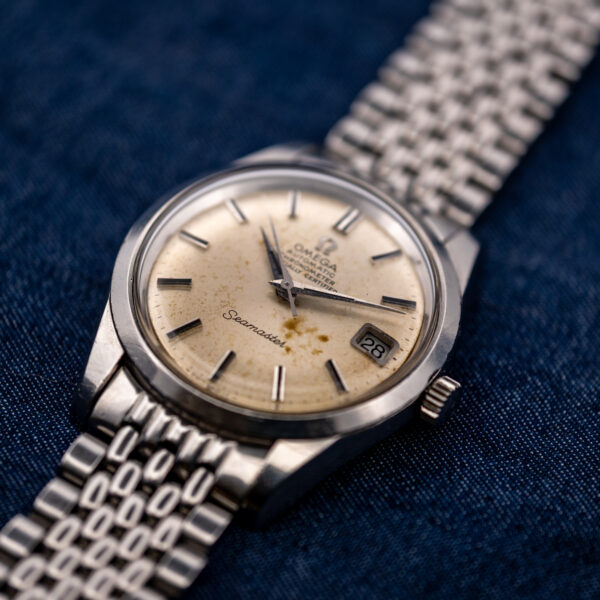 Omega Seamaster crown-side angle showing date aperture, pointed hands and bracelet end links beside raised crystal