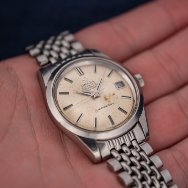 Omega Seamaster 166.010 held at an angle, with chronometer dial and multirow bracelet supported in hand