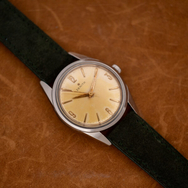 Zenith angled portrait showing Arabic quarter-hour numerals, pointed hands and stitched forest green suede strap